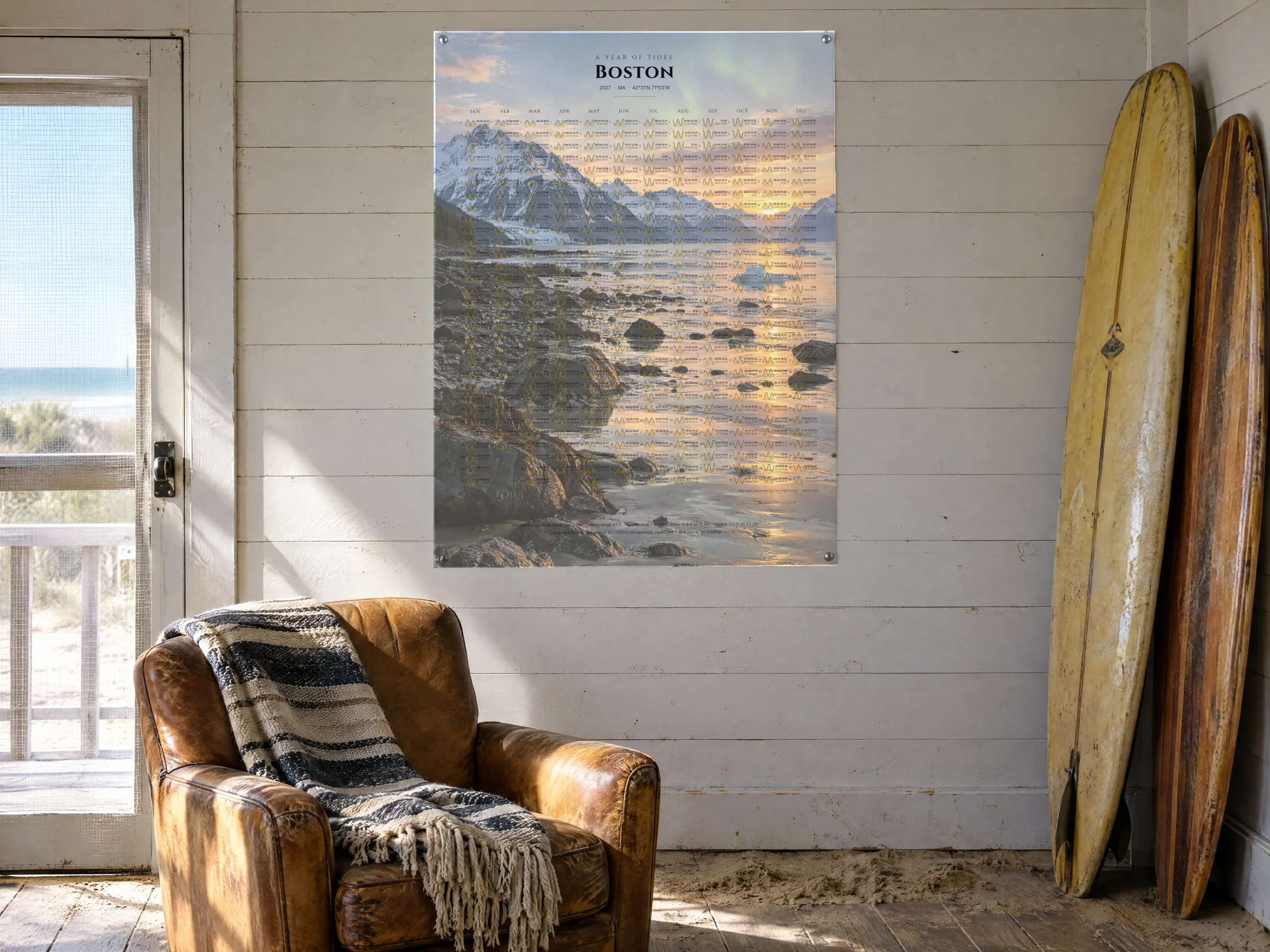 An unframed print of a year of tides over a surf photograph, pinned with brass pins to the plank wall of a surfer's bungalow beside two longboards