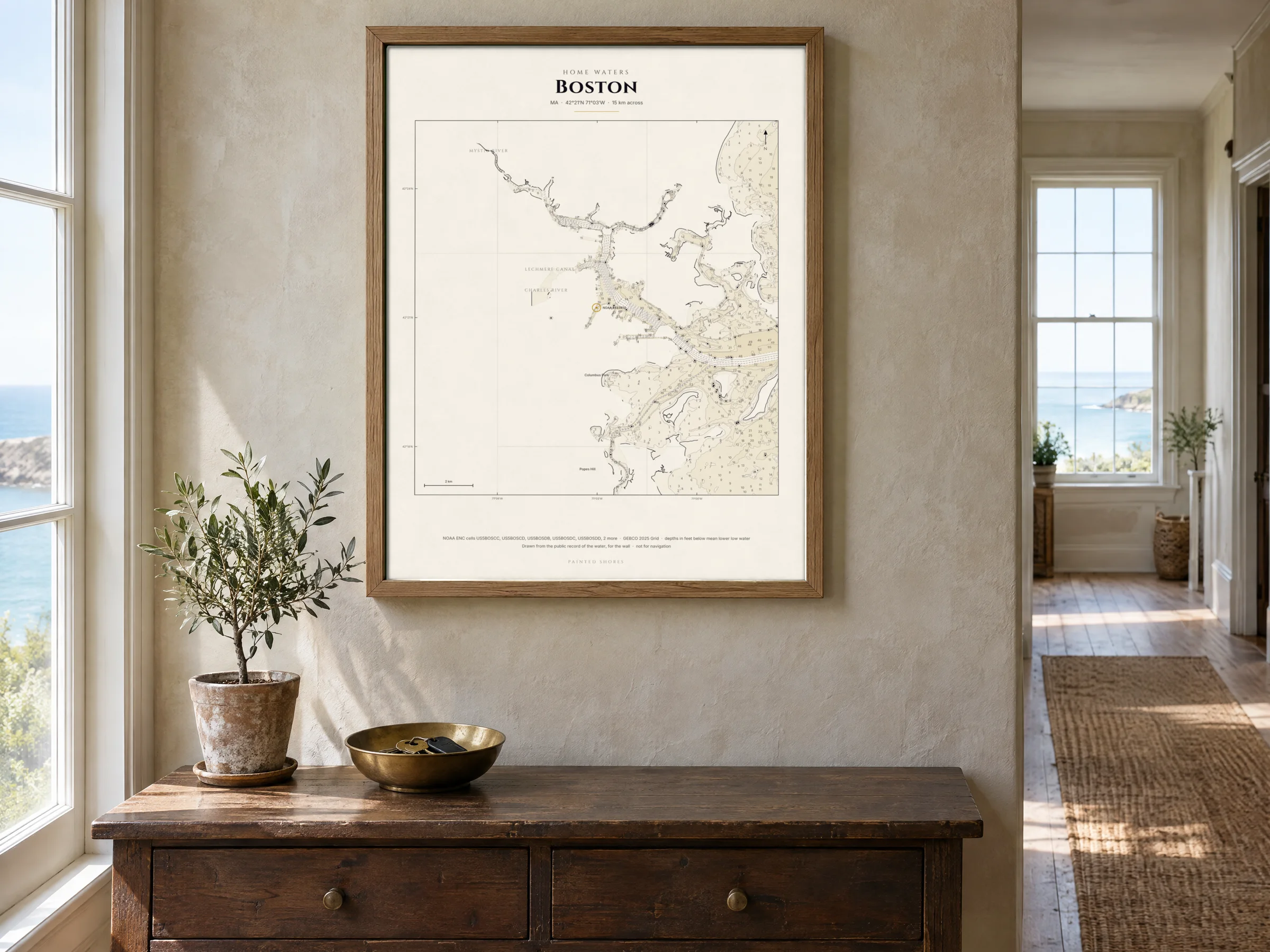 The home-waters chart of Boston Harbor in a natural oak frame above an oak console and a brass bowl of keys, in a limewashed hall